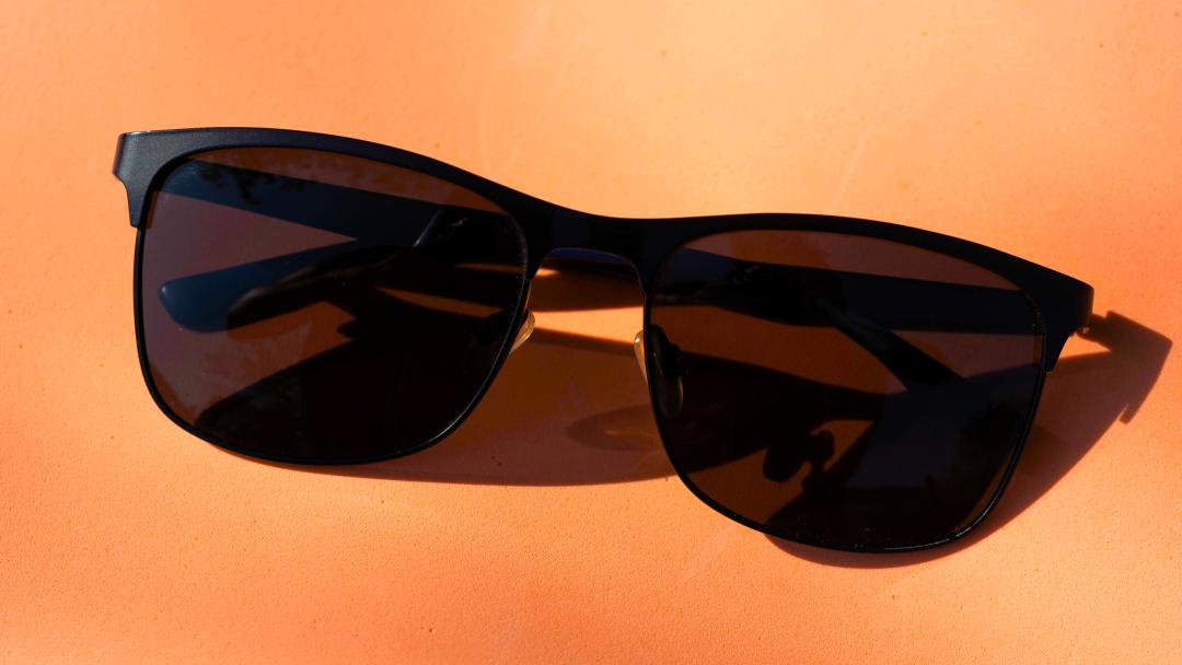 Auf einem orangen Hintergrund liegt eine schwarze Sonnebrille, die symbolisch für Anonymität steht. 